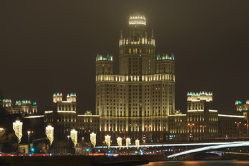 Wall Mural - Photography of Stalinist skyscraper on Kotelnicheskaya embankment, big traffic, stret filled out cars and bridge in winter night. The spire hiding in the fog. International touristic concepts.