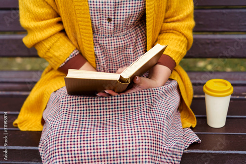 Fotografía A woman is sitting on a park bench and holding a book and bamboo cup with hot coffee