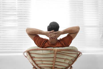 Wall Mural - Man relaxing in papasan chair near window at home, back view