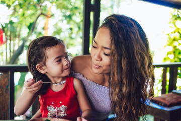 Attractive beautiful mother and cute little girl tasting food at restaurant