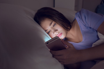 teenage girl with mobile phone lying in bed at night
