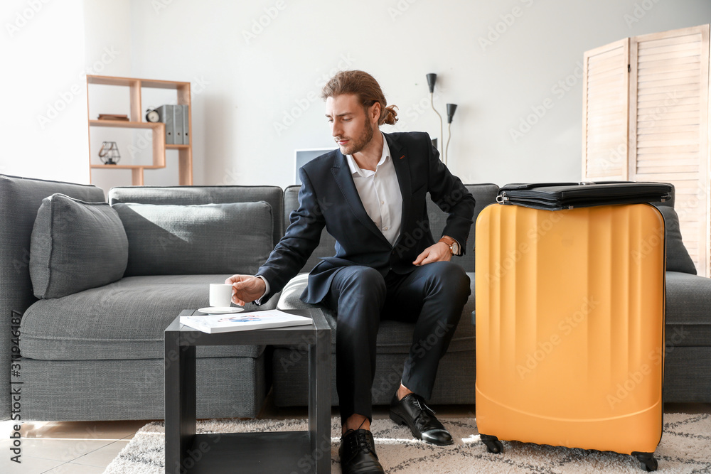 Young man with packed luggage for business trip at home