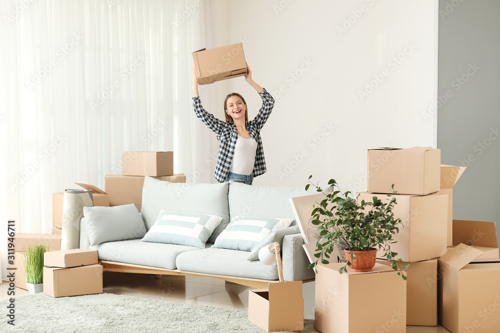 Happy young woman with moving boxes in new house