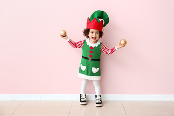 Canvas Print - Little girl in costume of elf and with Christmas balls near color wall