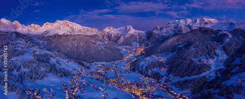 Beautiful panoramic view of Dolomites mountains at dusk during winter time. Magical winter mountain purple sunset with a mountain ski resort village. Christmas time.