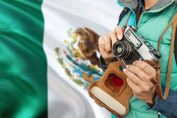 Wall Mural - Mexico photographer concept. Close-up adult woman holding retro camera on national flag background. Adventure and traveler theme.