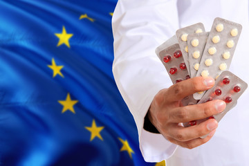 European Union pharmacy and medicine concept. Doctor holding pills tablet on national flag background. Health theme with copy space for text.