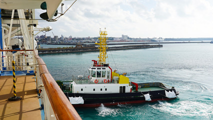 Wall Mural - A bright, powerful, new, industrial tug helps the ship maneuver in port. A tugboat helps moor a cruise ship in the clear blue water of tropical islands.v