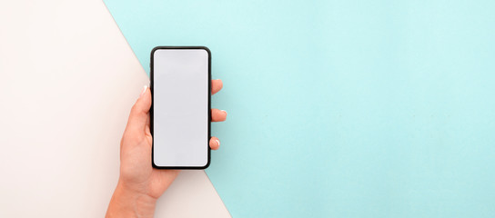 Woman hand holding the black smartphone with big blank screen and modern frame less design. Top view travel mockup horizontal banner