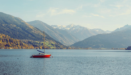 Wall Mural -  Panoramic view of beautiful mountain landscape in Alps with Zeller Lake in Zell am See, Salzburger Land, Austria. Red yaht at calm water Wonderful Lake. under bright sunlight