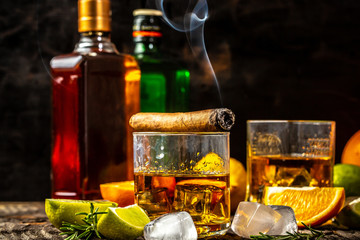 Hand alcoholic. concept of alcoholism, loneliness, dependence. A bottle of whiskey, a glass of whiskey and with ice, a cigar with smoke on a black table. Elite drink for masculine relaxation