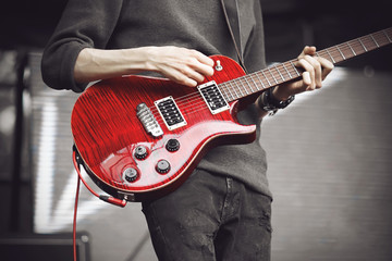 Wall Mural - A guitarist in a grey sweater and dark jeans with a bright red electric guitar plays a powerful track on stage at a rock concert.