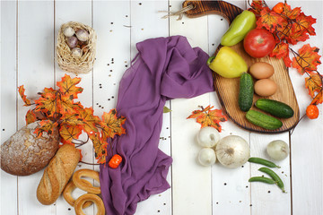 Autumn still life with bakery and vegetables on a board on a white wooden table, near orange maple leaves and purple cloth