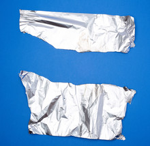 Two Torn Silver Pieces Of Baking Foil On A Blue Background