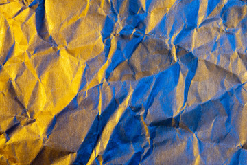 A close up abstract macro photo of crumpled creased paper lit with blue and orange flash gels