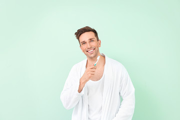 Sticker - Handsome man in bathrobe cleaning teeth on color background