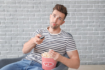 Sticker - Displeased man watching movie while sitting in armchair near grey wall