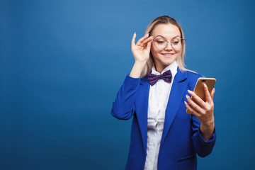 Wall Mural - Cute and funny businesswoman in a stylish blue jacket and bow tie uses a smartphone.