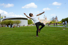 Young Man With Sunglasses, Jeans And White T-shirt, Jumping In The Grass. A Sunny Day In Museumplein The Museum Park In Amsterdam, Holland. People Outdoors In Spring.