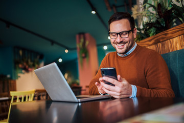 portrait of a smiling man using smart phone and laptop in the cafe.