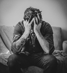 Distressed Man Sits on Couch with Head in Hands