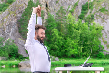 a man sits at a table on nature with his hands clasped up. office work and relaxation concept