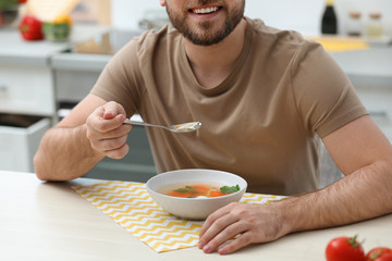 Poster - Young man eating tasty vegetable soup at table in kitchen, closeup