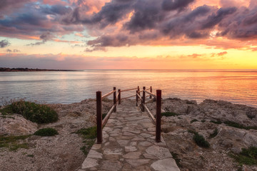 Wall Mural - Amazing colorful sunrise over the sea, rocks and stone stairs, scenic seascape, Cavo Greko, Ayia Napa, Cyprus. Outdoor travel background