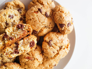 Homemade oatmeal cookies with pecan nuts and milk chocolate on a light grey plate on a white background