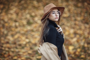 Image-shot of a young attractive woman wearing a coat and felt hat on blurry background of fallen leaves in the autumn park