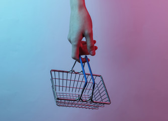 Wall Mural - Shopping concept. Female hand holds shopping basket..Creative pop art pink blue neon color. Trendy gradient illumination. Night light