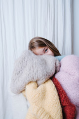 Wall Mural - Little girl is hugging pile of soft fluffy multi-colored freshly washed sweaters, aside from the color identical in every regard to the one she's wearing. At home, in front of a curtain.