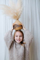 Wall Mural - Portrait of a cheerful little girl playing with coconut vase with cereal bouquet in it. She puts it on top of her head, for fun, or to show of her balance. At home, in front of a curtain.