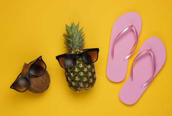 Summer background. Fun and humor concept. Beach resort. Pineapple and coconut with sunglasses, flip flopson yellow background