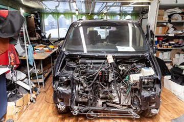 Wall Mural - Disassembled black car in the workshop prepared for repair: front end, hood and bumper removed, internal equipment, parts and spare parts visible. Auto service industry.