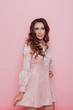 Portrait of a beautiful fashionable woman with hair curls in a pink dress on a pink background