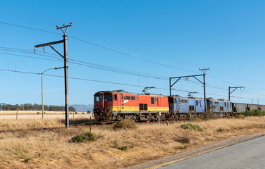 Hermon, South Africa. December 2019. Freight trains hauling wagons through countryside with a mountains backdrop.