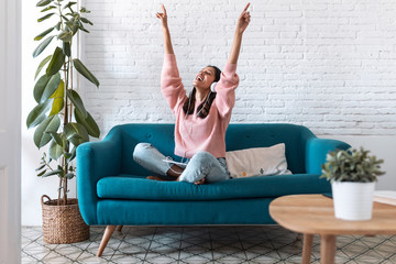 Motivated young woman listening to music with digital tablet while sitting on sofa at home.