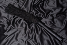 Black Whip On A Black Silk Background. Accessories For Adult Sexual Games