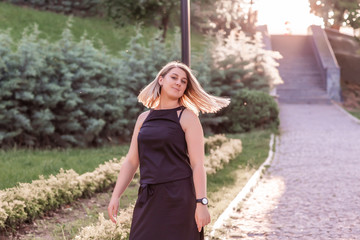 A blonde longhair student girl in black clothes walks in a green summer Park