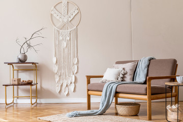 Stylish interior of living room at cozy apartment with brown sofa, coffe table, bookstand, white macrame and elegant accessories. Beige and japandi concept. Modern home staging. Template.