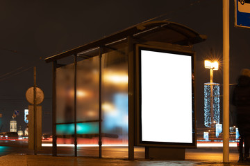 Canvas Print - Billboard in a stop. White field for advertising glowing at night in the city. Vertical Field Mockup glass stop passing by blurry cars with people in the background