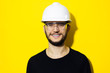 © Lalandrew - Studio portrait of young smiling man architect, builder engineer, wearing black sweater, white construction safety helmet and glasses isolated on yellow background.