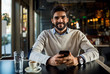 © Novak - Handsome young beard man in cafe using smart phone and smiling