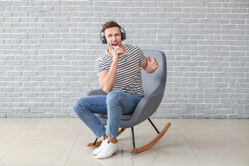 Poster - Handsome man listening to music while sitting in armchair near grey wall