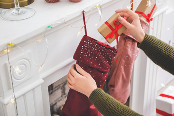 Canvas Print - Woman putting gifts into Christmas socks hanging on fireplace at home