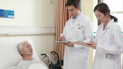 Wall Mural - two young asian doctors making rounds informing worried senior patient of seriousness of his medical condition