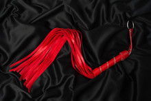 Red Whip On A Black Silk Background. Accessories For Adult Sexual Games