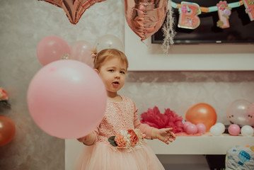 2 year baby girl in pink dress with her first birthday cake, happy birthday card,a cute little girl celebrates her first birthday surrounded by gifts