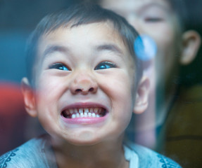 Curious child standing behind the glass and pressing his nose on a glass window